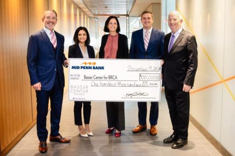 Five people smiling holding a $100,00.00 life-size check